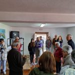 Grupo de pessoas de diferentes idades ouvindo atentamente um homem idoso em uma sala simples.